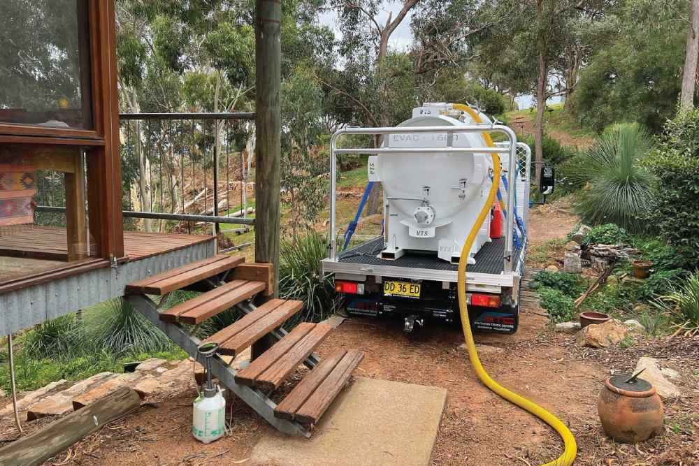 A Poo Carters vacuum truck performing a septic tank pump-out at a rural property, demonstrating their professional septic services-